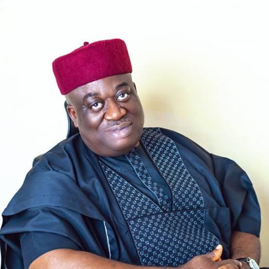 Smiling man in a maroon kufi cap and dark blue embroidered traditional West African attire.