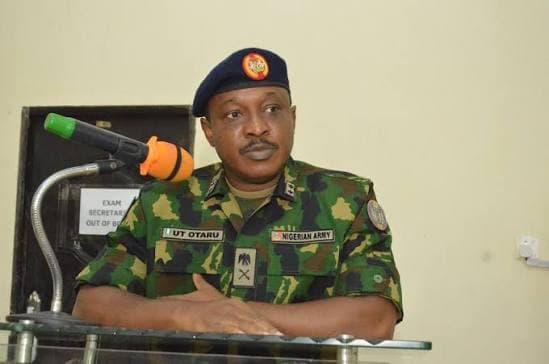 Nigerian Army officer in camouflage uniform and blue beret standing behind a podium microphone.